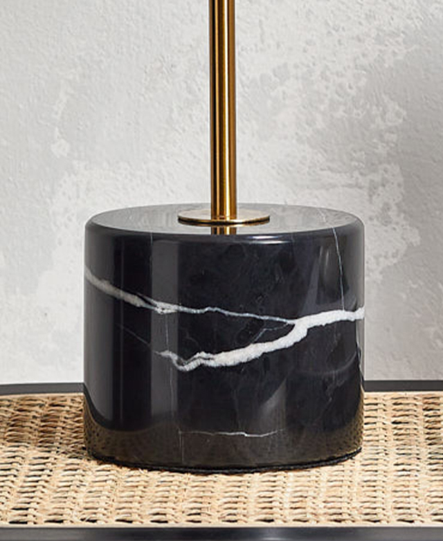 The round, black marble base of a lamp is shown, with intricate white veining throughout.