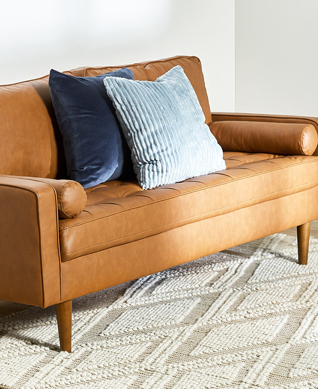 Two blue cushions are positioned in the middle of the sofa, which stands on top of a creamy diamond-patterned rug.
