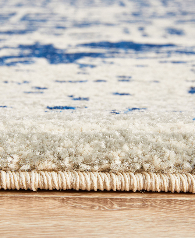 The 10mm pile height and thick, natural-toned serged edge around the perimeter of the rug are shown from up close.