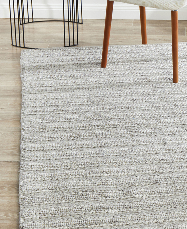 A neutral wool rug positioned above timber flooring.