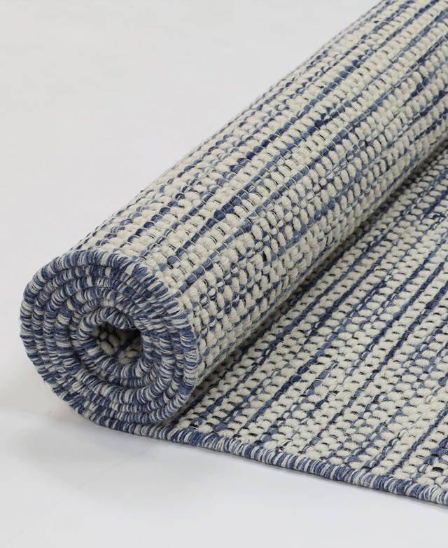 The blue and white wool rug is rolled up on the floor, highlighting its reversible design. The blue and white wool rug is rolled up on the floor, highlighting its reversible design.