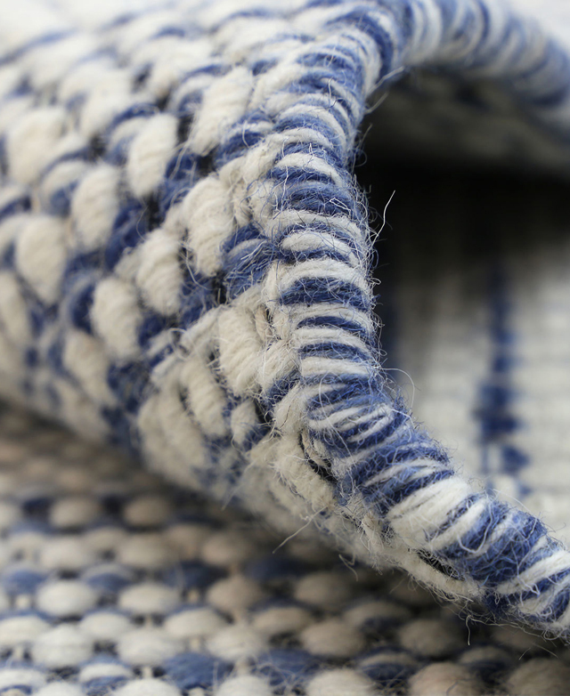 Close-up of the rug's wool texture and thick white and blue serged edge. Close-up of the rug's wool texture and thick white and blue serged edge.