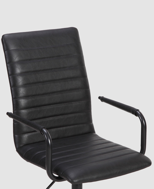 From a side angle, a chair with horizontal stitching on faux leather upholstery is shown. From a side angle, a chair with horizontal stitching on faux leather upholstery is shown.