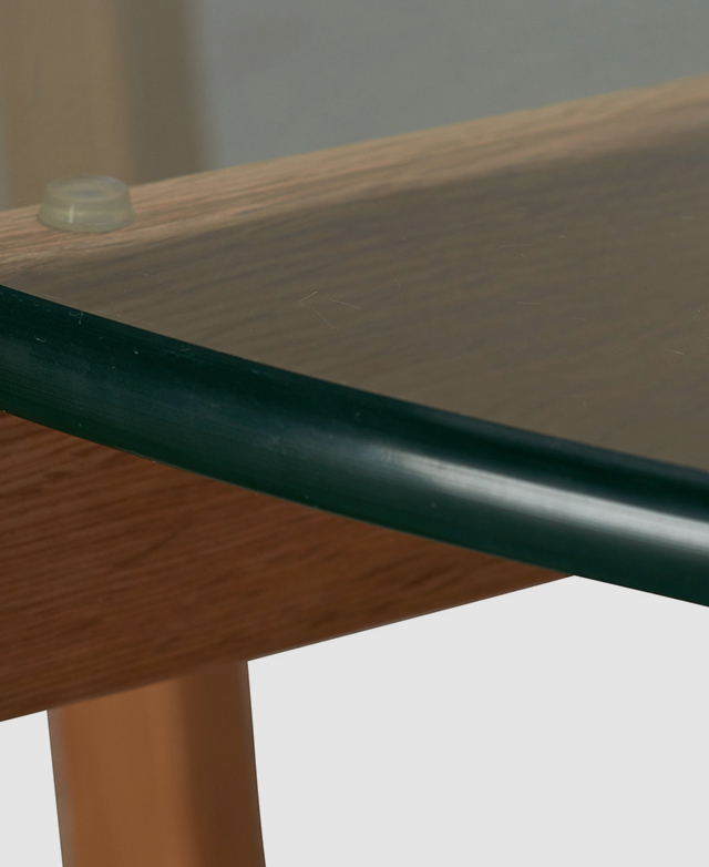 Close up of the smooth edge of a coffee table's tempered glass top resting on a timber frame.