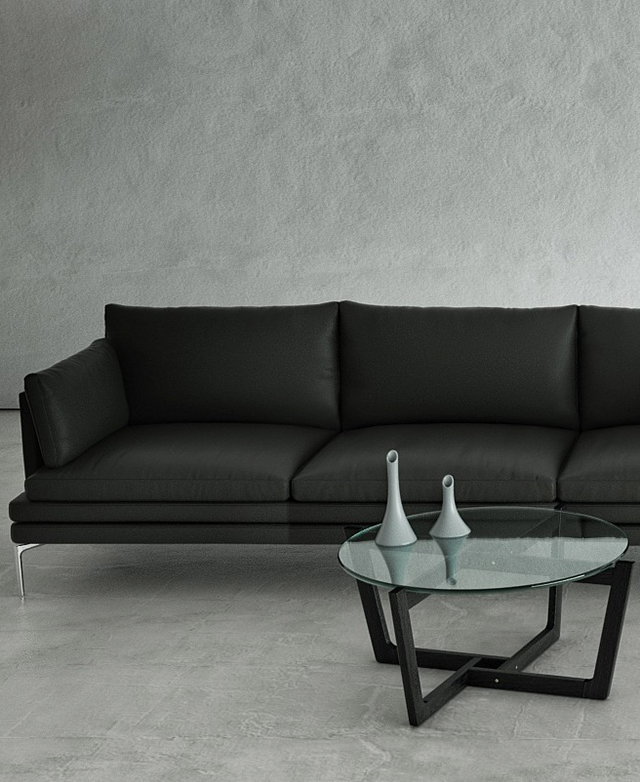 A coffee table with a round glass top and black geometric base is styled in front of a black leather sofa.