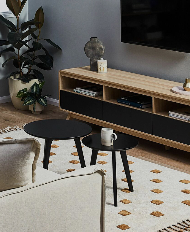 A set of two black timber nesting tables positioned next to each other in front of an entertainment set-up in a living room.