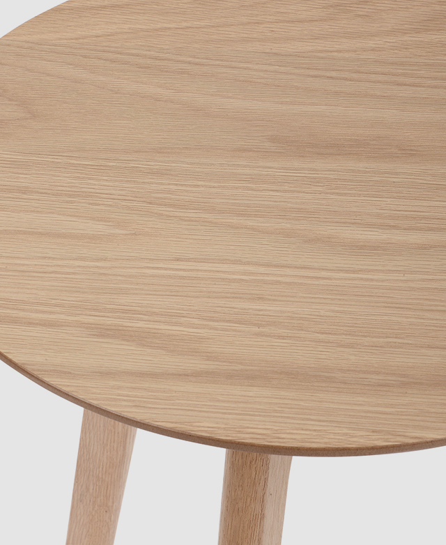 Close up of the top of a round side table, highlighting the typically straight wood grain of the oak veneer.