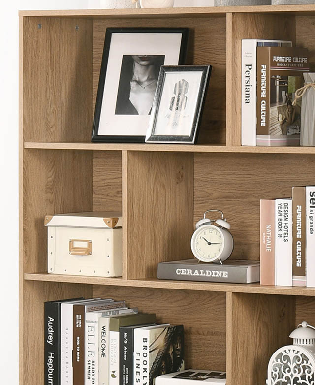 Various books and decor items are arranged on the shelving units of a light oak coloured bookcase.