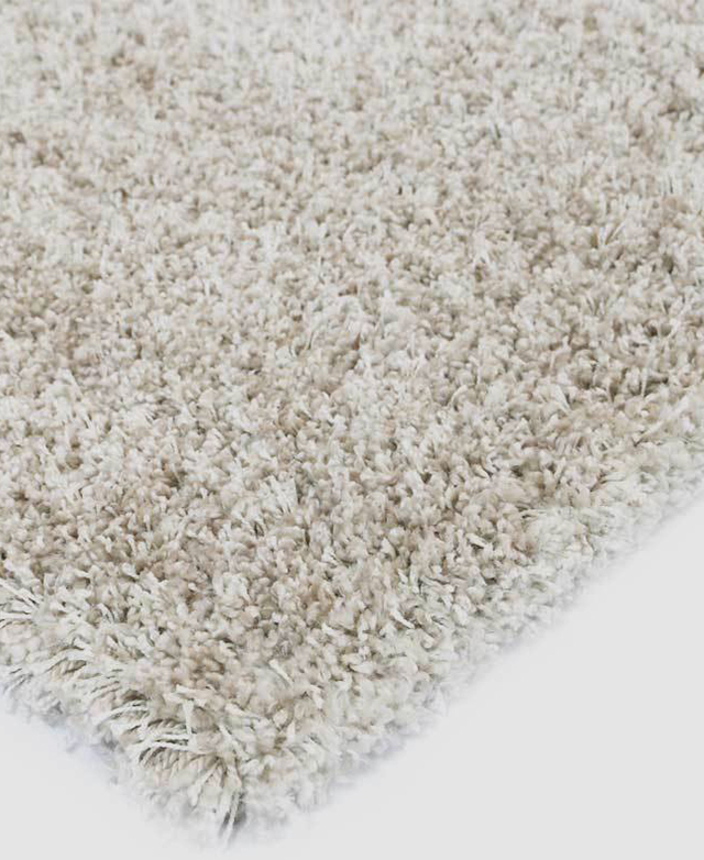 A corner of a power-loomed rug in a neutral colour and with long shaggy fibres.