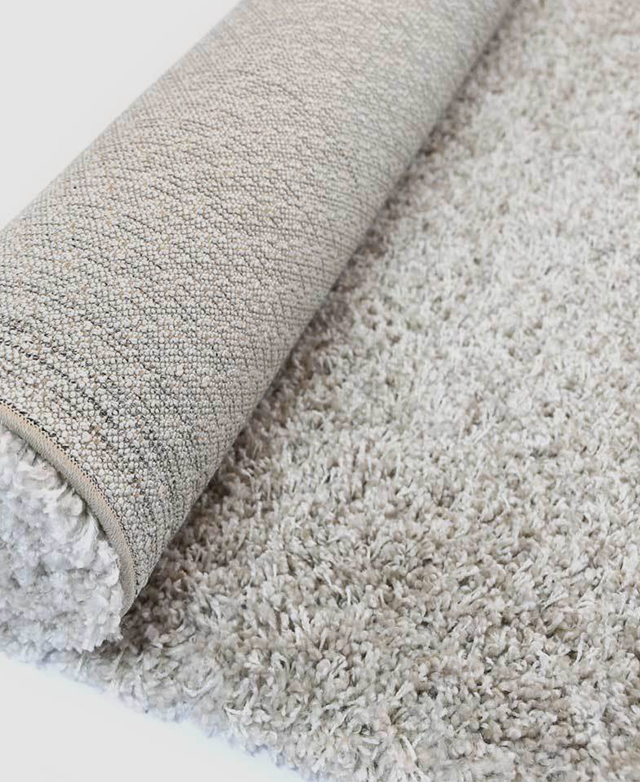 A shag rug is partially rolled up on the floor. On the underside is a thick and durable jute backing.
