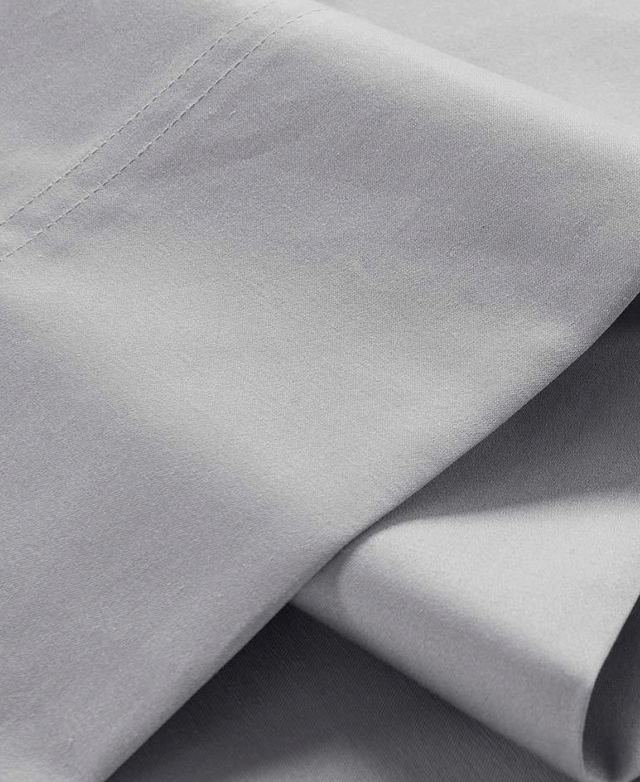 Close view of the top end of a flat sheet in a light grey colour shows the elegant double-stitch trim.