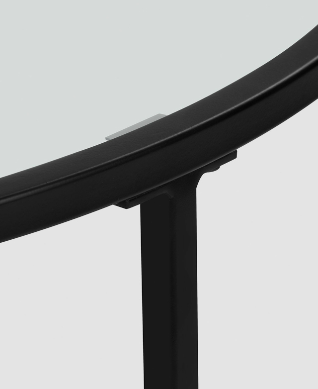 A close-up shows the detail of the simple black steel frame and small section of the clear glass top. A close-up shows the detail of the simple black steel frame and small section of the clear glass top.