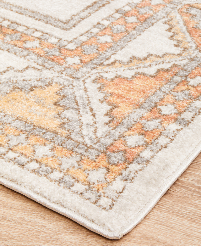 Creams & soft shades of orange are shown at the corner of the rug, close up. The edges are tightly bound.