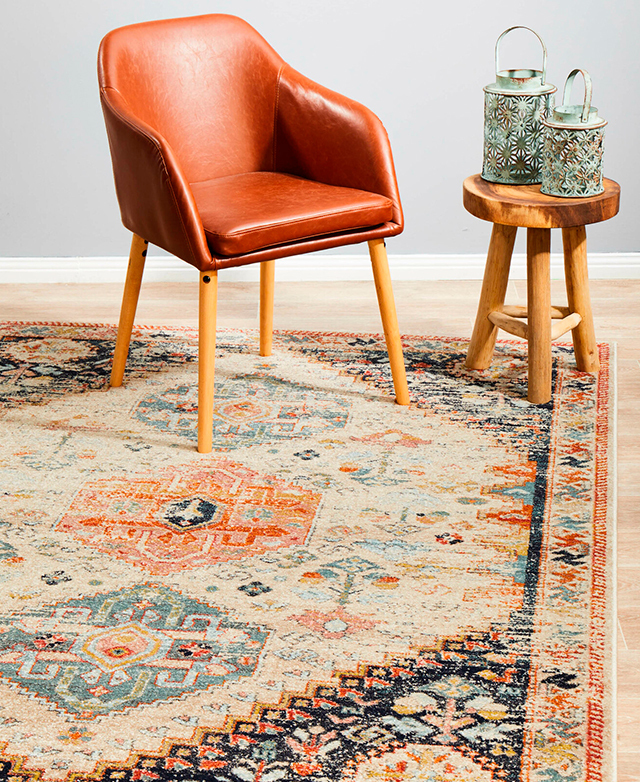 The ornate rug is shown with a modern tan leather armchair and a wood side table on top.