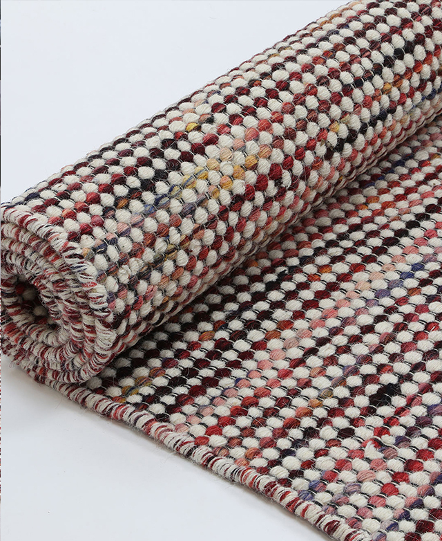 A colourful wool rug is rolled up on the floor, highlighting its reversible design.