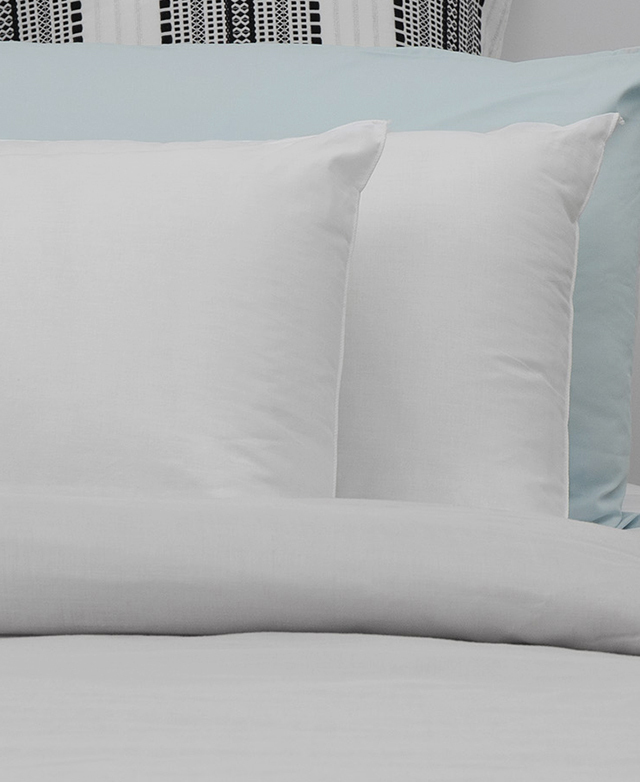Two plush pillows styled in front of each other on a bed with white sheets. Two plush pillows styled in front of each other on a bed with white sheets.