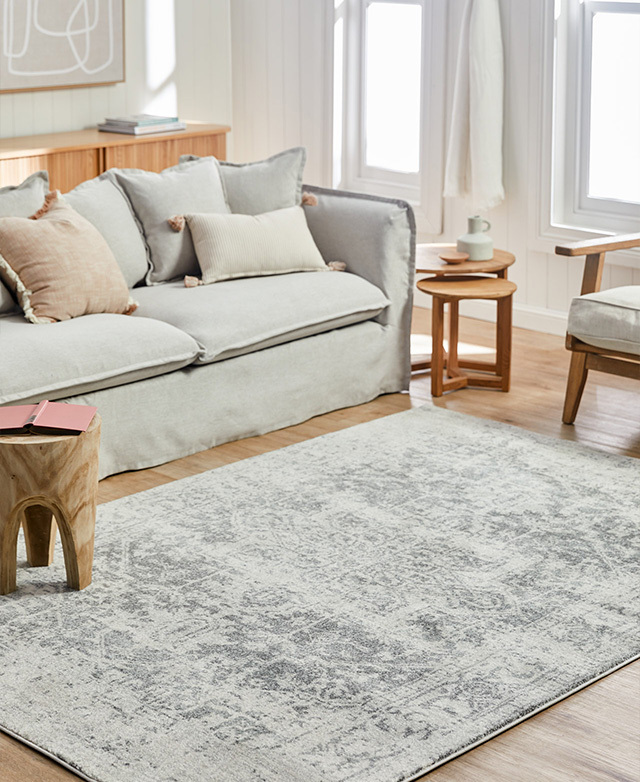 The rug is in a living room, surrounded by a light grey sofa, a modern chair and side tables.