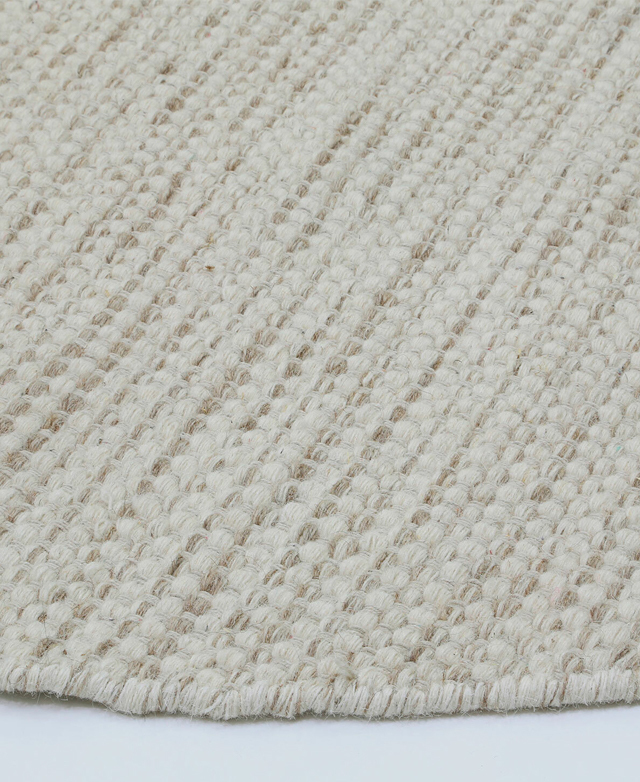 Side view of the round wool-blend rug, highlighting its tufted texture and thick woven border. Side view of the round wool-blend rug, highlighting its tufted texture and thick woven border.