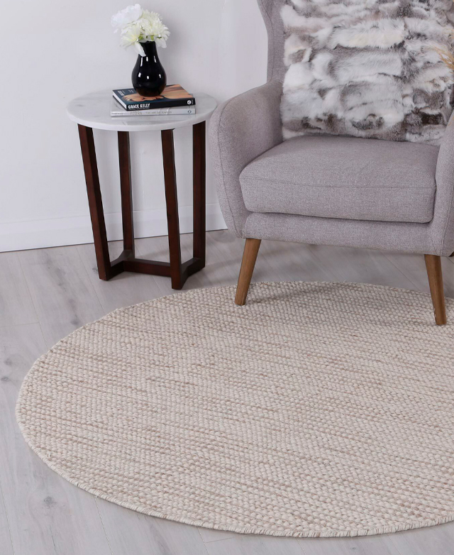 The circular wool rug in situ in a classic space, underneath a grey armchair and marble side table. The circular wool rug in situ in a classic space, underneath a grey armchair and marble side table.