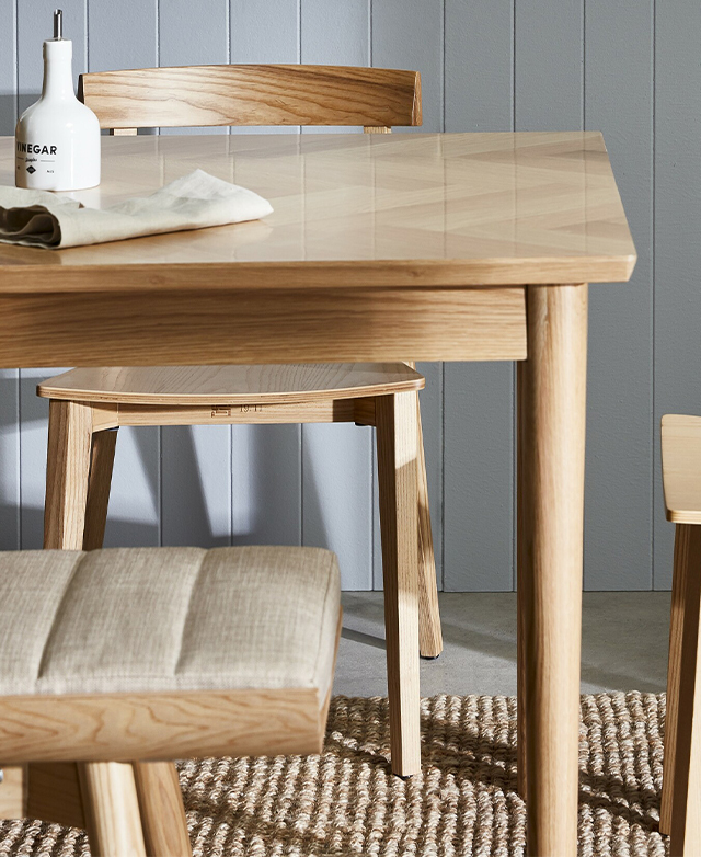 A soft grey panelled wall is in the background; the foreground holds the blonde table and coordinating seating. A soft grey panelled wall is in the background; the foreground holds the blonde table and coordinating seating.
