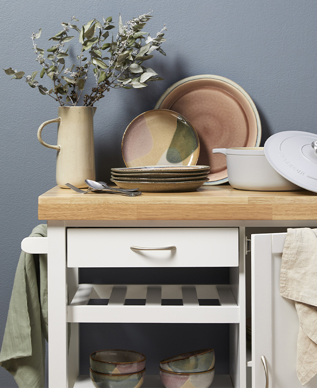 Earthenware and a vase of dried foliage sit on top of the kitchen trolley, enhancing its rustic appeal.