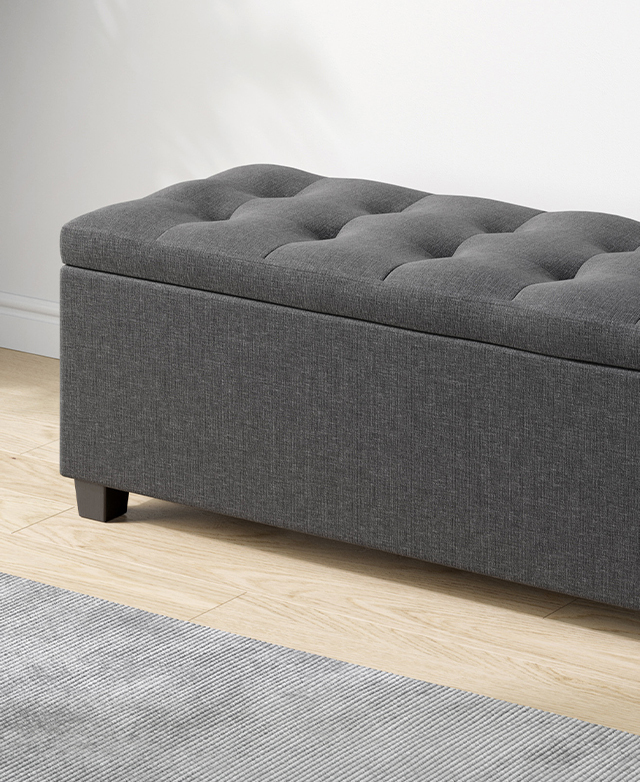 The charcoal ottoman is on a light timber floor, and a light grey ribbed rug is just in shot.