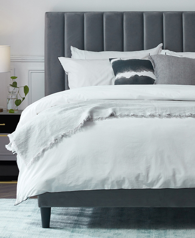 The bedhead is positioned behind a bed that's dressed with layers of linen in light, cool tones.