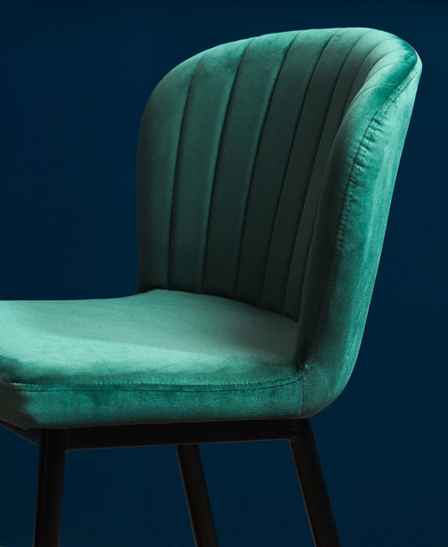 Side profile of a velvet green high back bar stool with channel-tufted details on the curved seat.