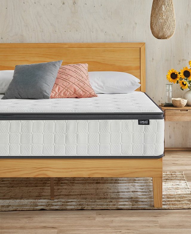 The undressed mattress is on a simple wooden bed frame, which is positioned next to a side table with sunflowers on top.