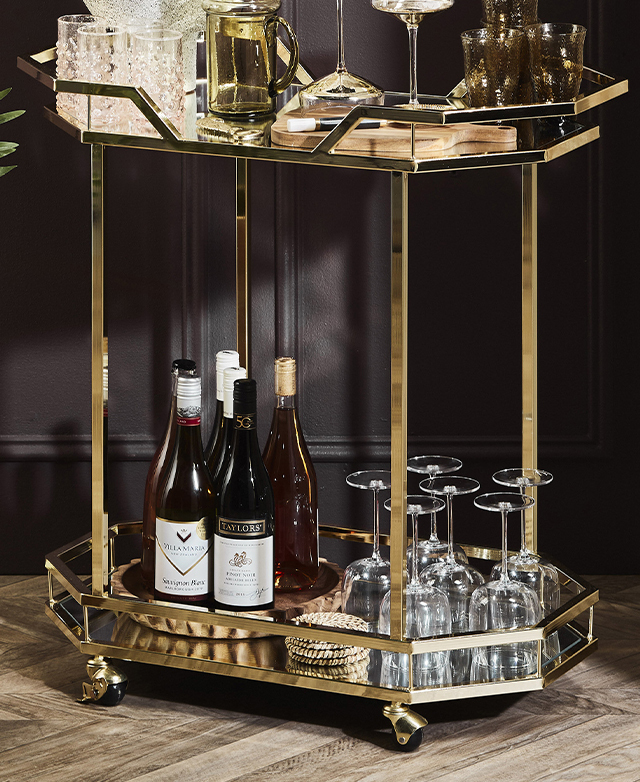 A slight angle displays the full bar cart with a range of glassware and wine bottles on the top and bottom shelves.