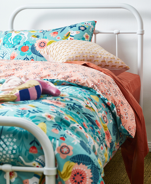 Brightly coloured bedding, complete with pillow and cushion, is seen against the simple bedhead.