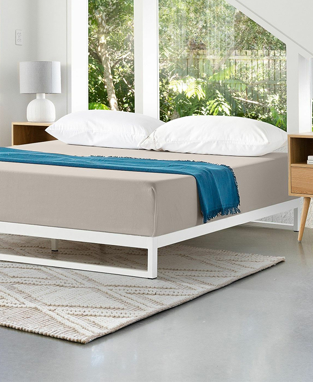 The bed base is shown with a neatly dressed mattress on top, in a bright room.