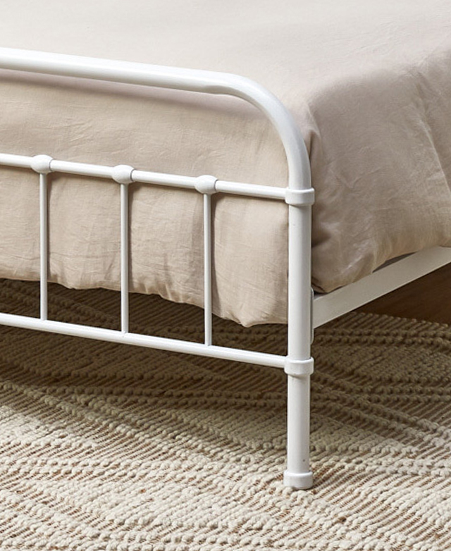 A cropped three-quarter image shows the crisp white frame complementing simple taupe bedding and a creamy, textured rug.