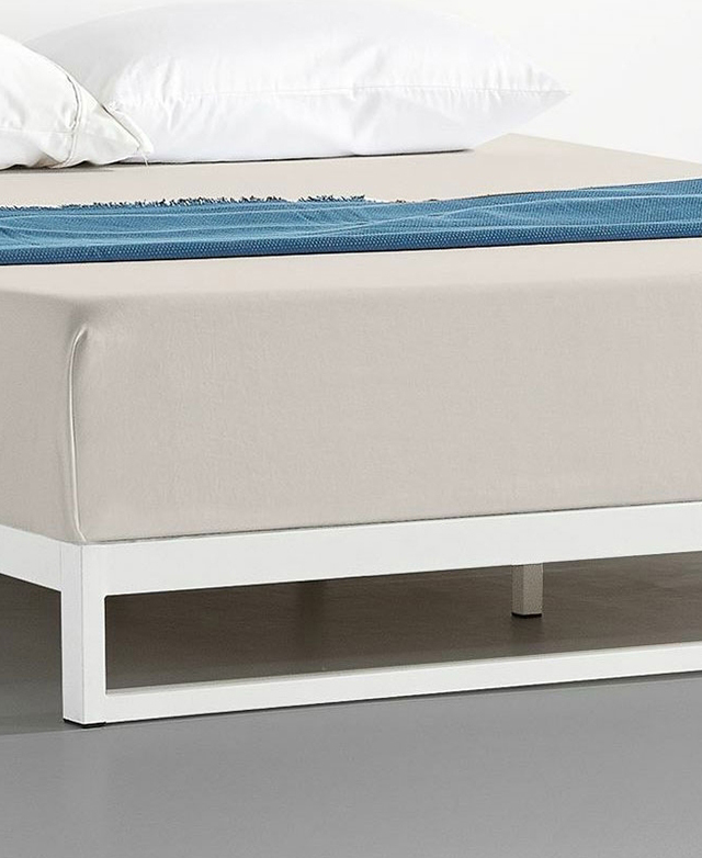 Up close is the simplicity of the low, square tube bed frame. A sheet-covered mattress is on top.