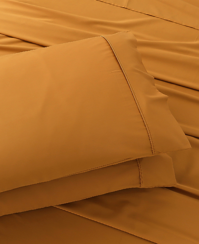 Close-up of a pair of deep orange pillows stacked on top of a bed. A neat double stitch adorns the pillowcase cuff. Close-up of a pair of deep orange pillows stacked on top of a bed. A neat double stitch adorns the pillowcase cuff.