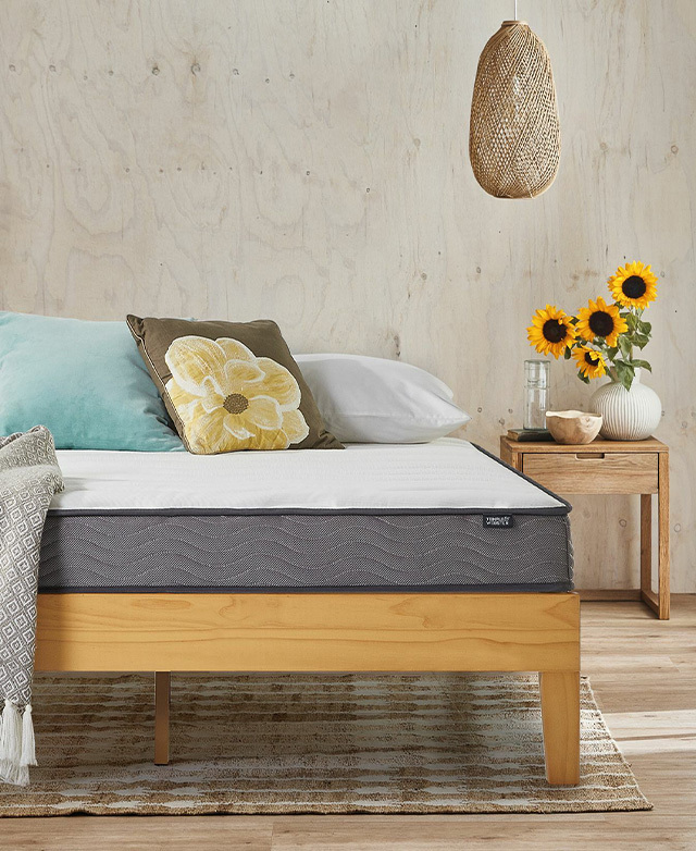 A mattress on a timber bed frame. A vase of blooming sunflowers is on the adjacent bedside table.