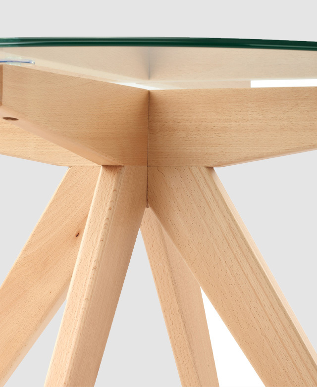 The blonde beech wood base just beneath the glass top is presented at eye level. Natural wood grains evident. The blonde beech wood base just beneath the glass top is presented at eye level. Natural wood grains evident.
