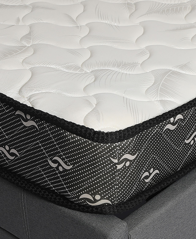 A corner of the mattress is shown on top of a grey upholstered bed.