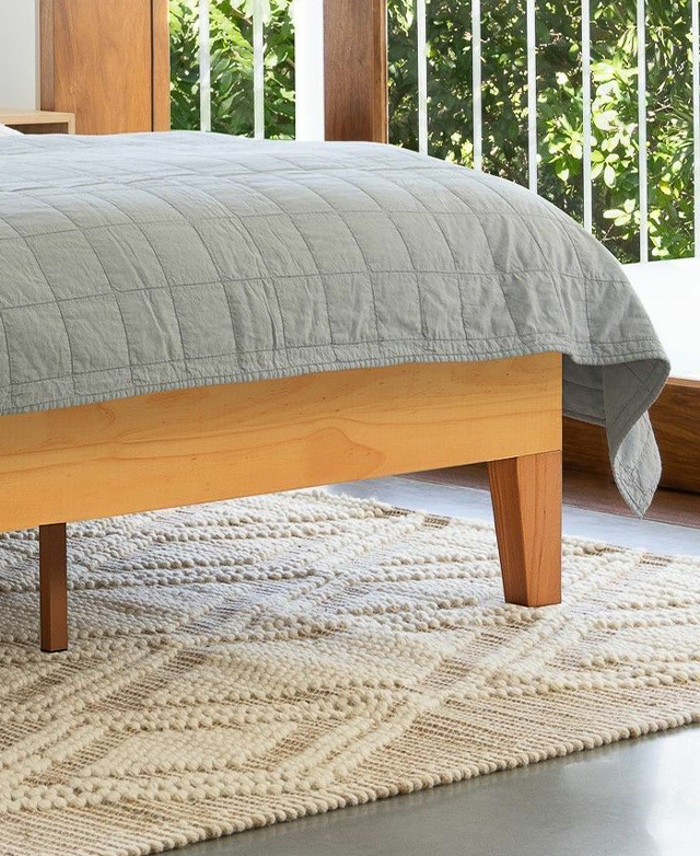 Yellow undertones of the bed base are enhanced with the cool tones of a light grey panel-stitched coverlet on top. Yellow undertones of the bed base are enhanced with the cool tones of a light grey panel-stitched coverlet on top.