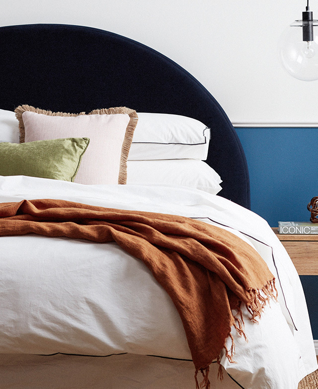 A cosy bed with a white quilt and navy blue velvet bedhead.