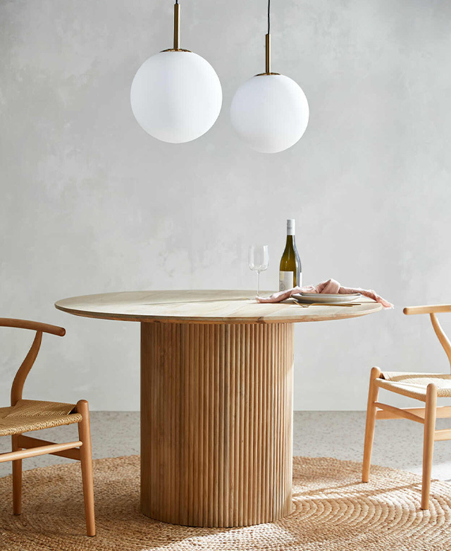 The dining table stands in the centre of a round jute rug, beneath a pair of white, spherical pendant lights.