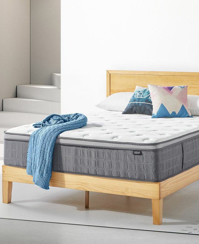 The mattress is situated on a blonde timber bed. A blue knitted blanket, two cushions and pillows are on top.
