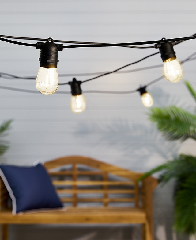 Rows of illuminated festoon lights are in focus, strung up above an outdoor entertaining area.