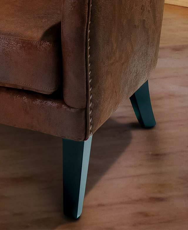 Oak wood legs in a dark finish are tapered and splayed underneath the brown armchair. Oak wood legs in a dark finish are tapered and splayed underneath the brown armchair.