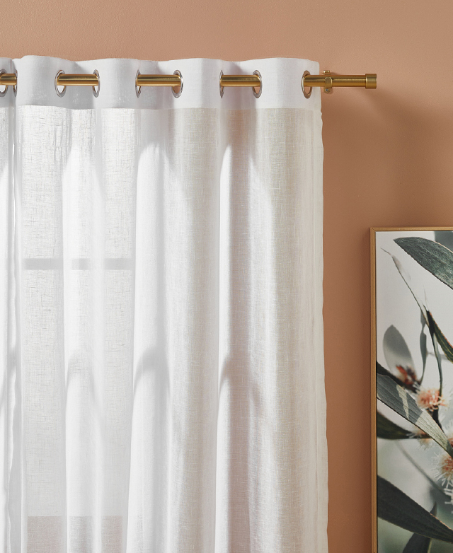 A sheer white curtain hangs off of a curtain rod with a soft brass finish.