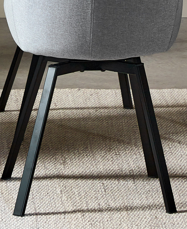 Angular black metal legs are anchored on a cream, woven rug. Angular black metal legs are anchored on a cream, woven rug.