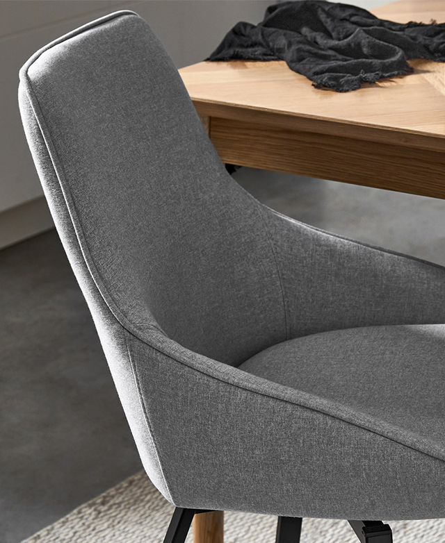 A slightly elevated side view depicts the curved, tapering armrests and the piping trim. A slightly elevated side view depicts the curved, tapering armrests and the piping trim.
