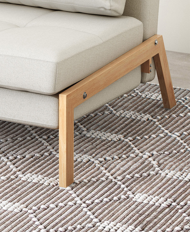 A sofa with a timber-look finish on the steel legs is styled atop a textured rug. A sofa with a timber-look finish on the steel legs is styled atop a textured rug.