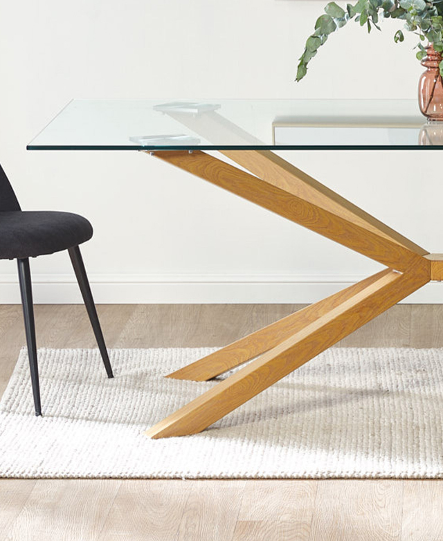 Half a rectangular dining table is cropped at an eye-level side view. It's styled above a textured white rug. Half a rectangular dining table is cropped at an eye-level side view. It's styled above a textured white rug.