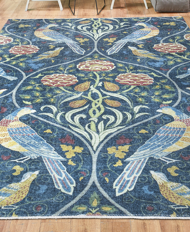 The rug is rolled out on a timber floor. The ornate details include birds, flowers and leaves.